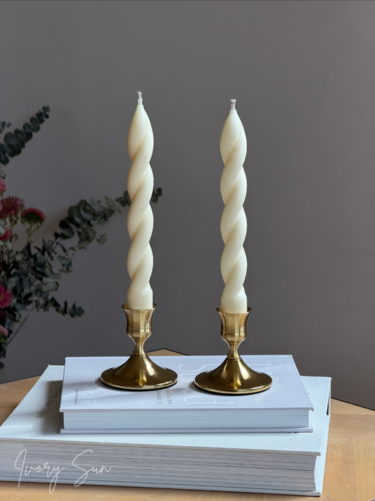 Two elegant gold candle holders Australia styled with twisted taper candles on a stack of books, creating a refined modern décor display. These metal candle holders with a golden finish are perfect for showcasing taper candles at weddings, dinner parties and special occasions. The Ivory Sun candle holder collection offers timeless candle accessories, including twin candle holders, wedding candle holders, dinner party candle holders and stylish table décor pieces.