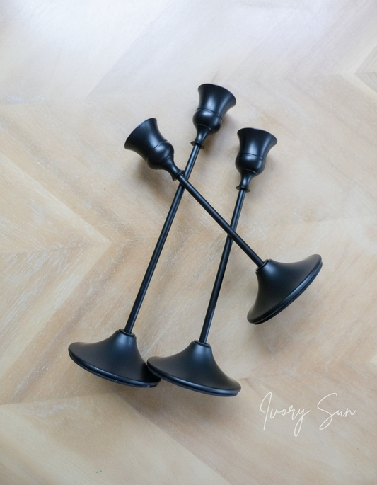 Set of three black candle holders on a wooden surface.
metal candle holders, black candle holders, black candle holders, candle holders australia, candle holder, candle holder australia, ivory sun candle holder, candle accessories, wedding candle holders, dinner party candle holders, decor candle holders, twin candle holders, table decor, taper candles, candle holders set