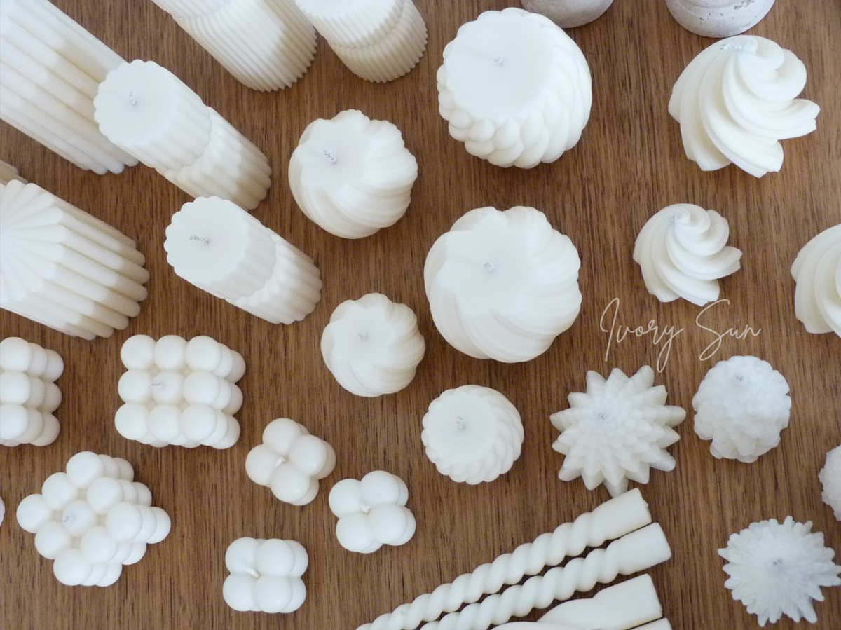 Assorted soy wax sculptural and pillar candles on a wooden surface, handmade by Ivory Sun.