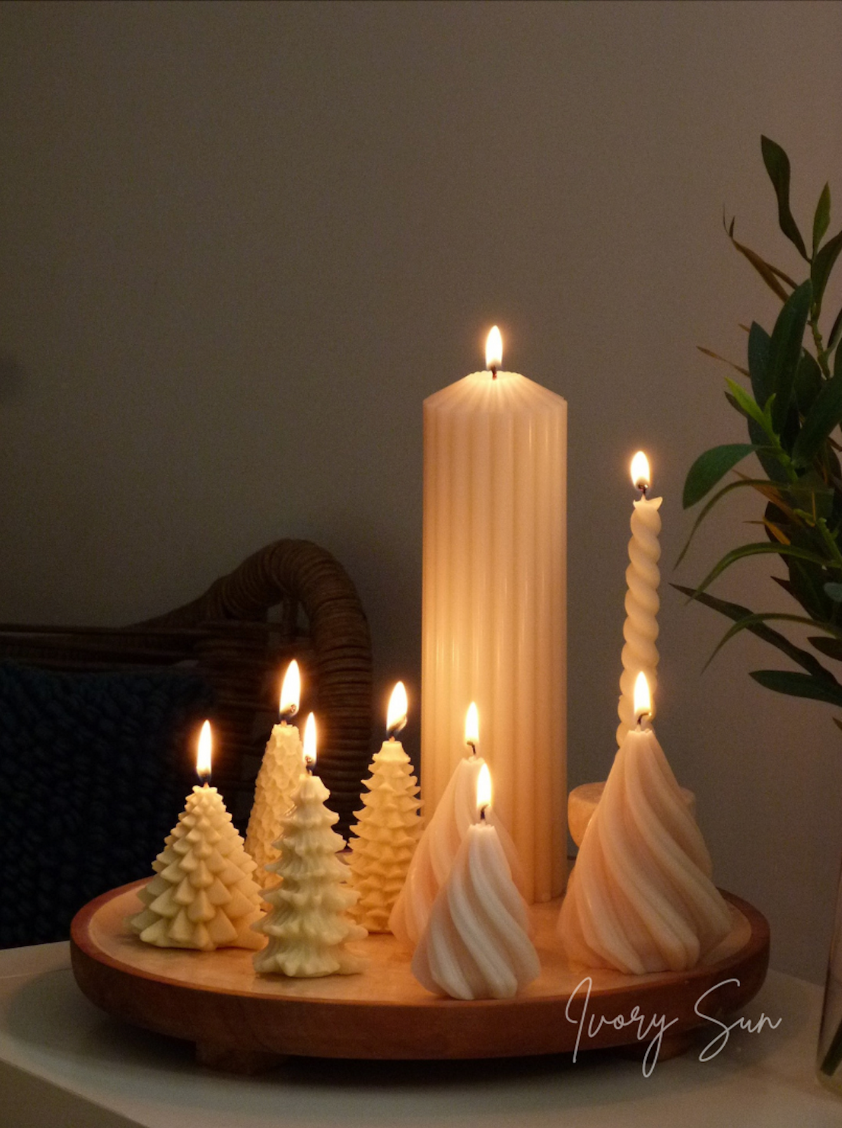 Decorative tree shaped Christmas candles on a wooden tray with a plant in the background. Handmade sculptural candles by Ivory Sun.