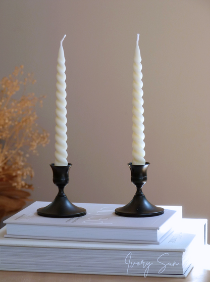 Two white twisted candles in black candle holders on a stack of books with a beige background.
metal candle holders, black candle holders, black candle holders, candle holders australia, candle holder, candle holder australia, ivory sun candle holder, candle accessories, wedding candle holders, dinner party candle holders, decor candle holders, twin candle holders, table decor, taper candles, candle holders set