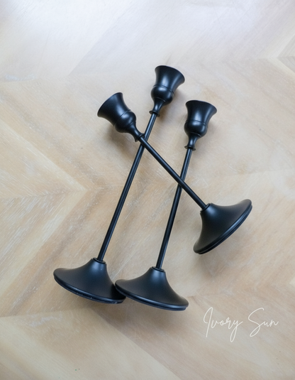 Set of three black candle holders on a wooden surface.
metal candle holders, black candle holders, black candle holders, candle holders australia, candle holder, candle holder australia, ivory sun candle holder, candle accessories, wedding candle holders, dinner party candle holders, decor candle holders, twin candle holders, table decor, taper candles, candle holders set