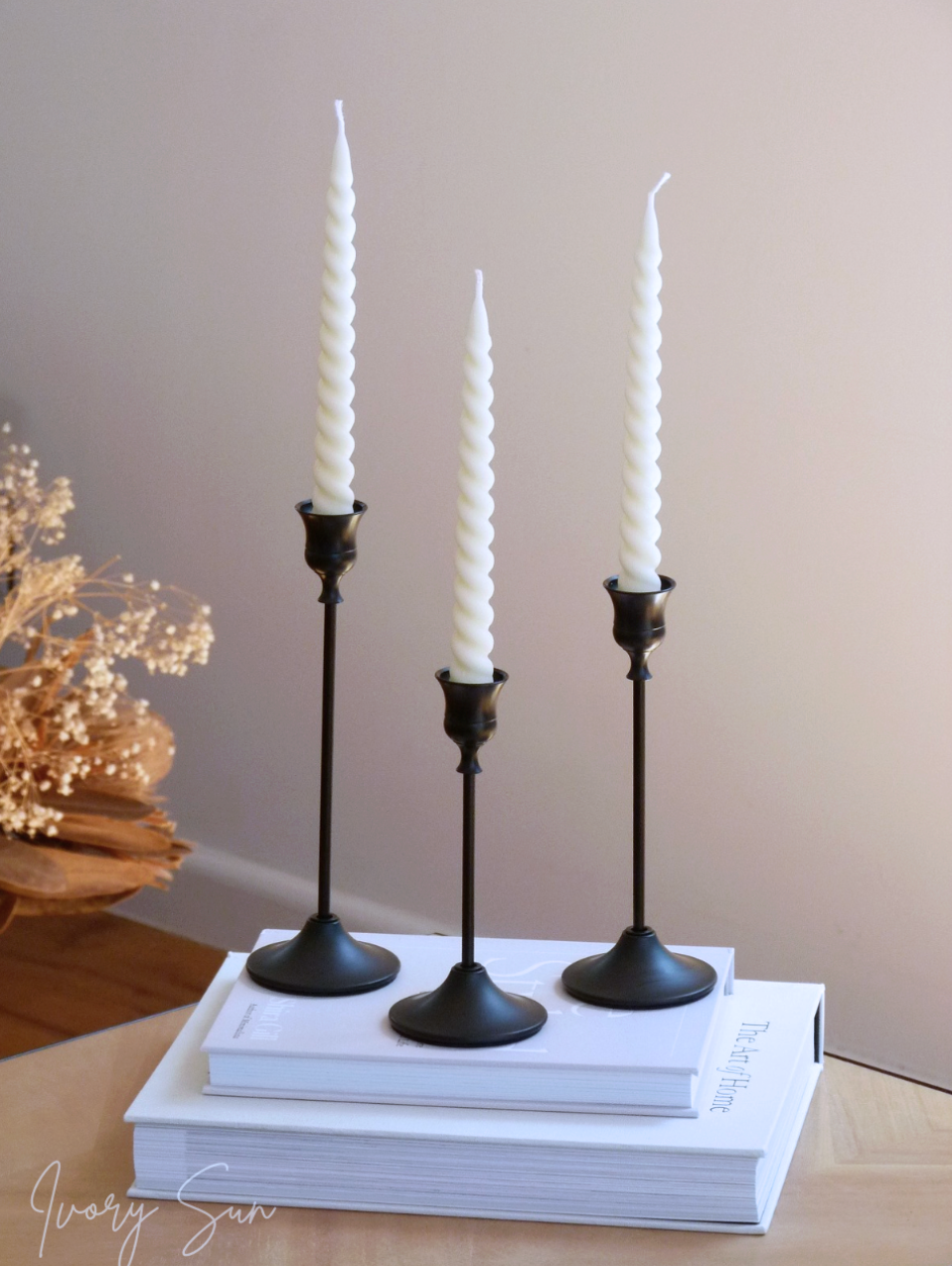 Three black candlesticks with white candles on a stack of books against a neutral background.
metal candle holders, black candle holders, black candle holders, candle holders australia, candle holder, candle holder australia, ivory sun candle holder, candle accessories, wedding candle holders, dinner party candle holders, decor candle holders, twin candle holders, table decor, taper candles, candle holders set