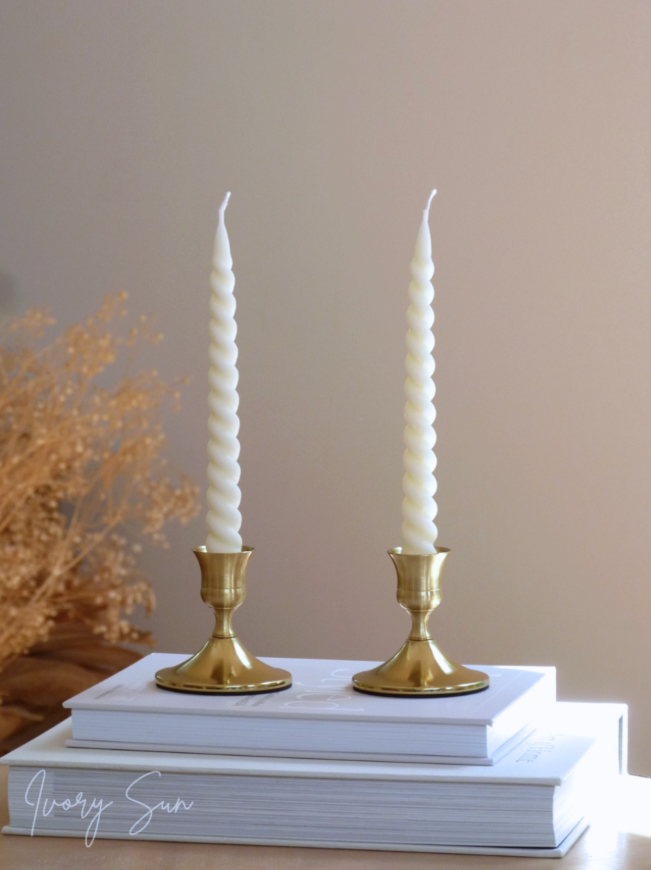 Two white candles in gold candle holders on a stack of books with a neutral background.
metal candle holders, gold candle holders, golden candle holders, candle holders australia, candle holder, candle holder australia, ivory sun candle holder, candle accessories, wedding candle holders, dinner party candle holders, decor candle holders, twin candle holders, table decor, taper candles, candle holders set