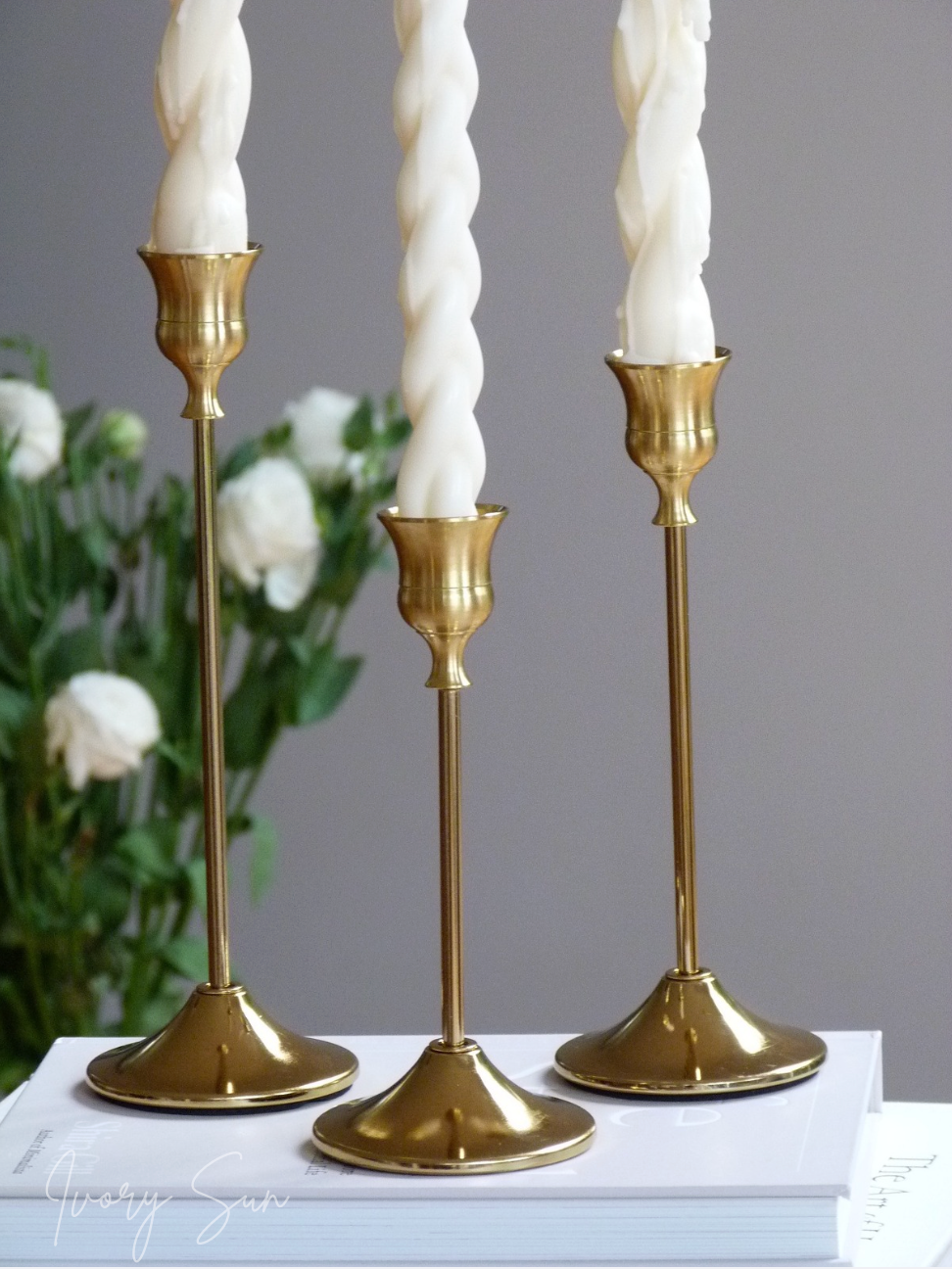 Three gold candlesticks with white taper candles on a gray background.
metal candle holders, gold candle holders, golden candle holders, candle holders australia, candle holder, candle holder australia, ivory sun candle holder, candle accessories, wedding candle holders, dinner party candle holders, decor candle holders, twin candle holders, table decor, taper candles