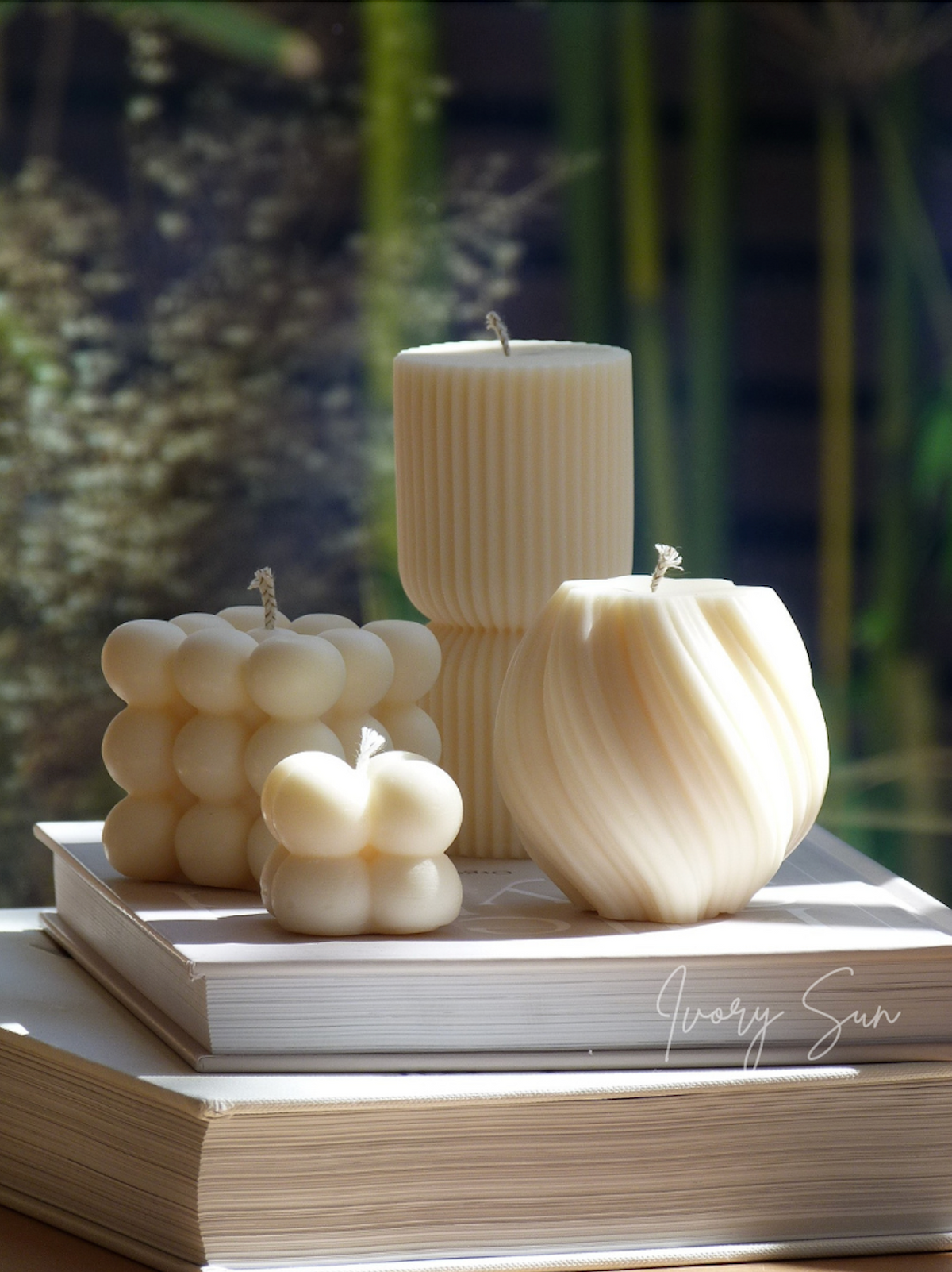 Set of decorative candles on a stack of books with a blurred natural background. Natural candles made from soy wax or Australian beeswax, with selected candles scented using 100% pure essential oils. Hand-poured in small batches in Sydney, Australia.