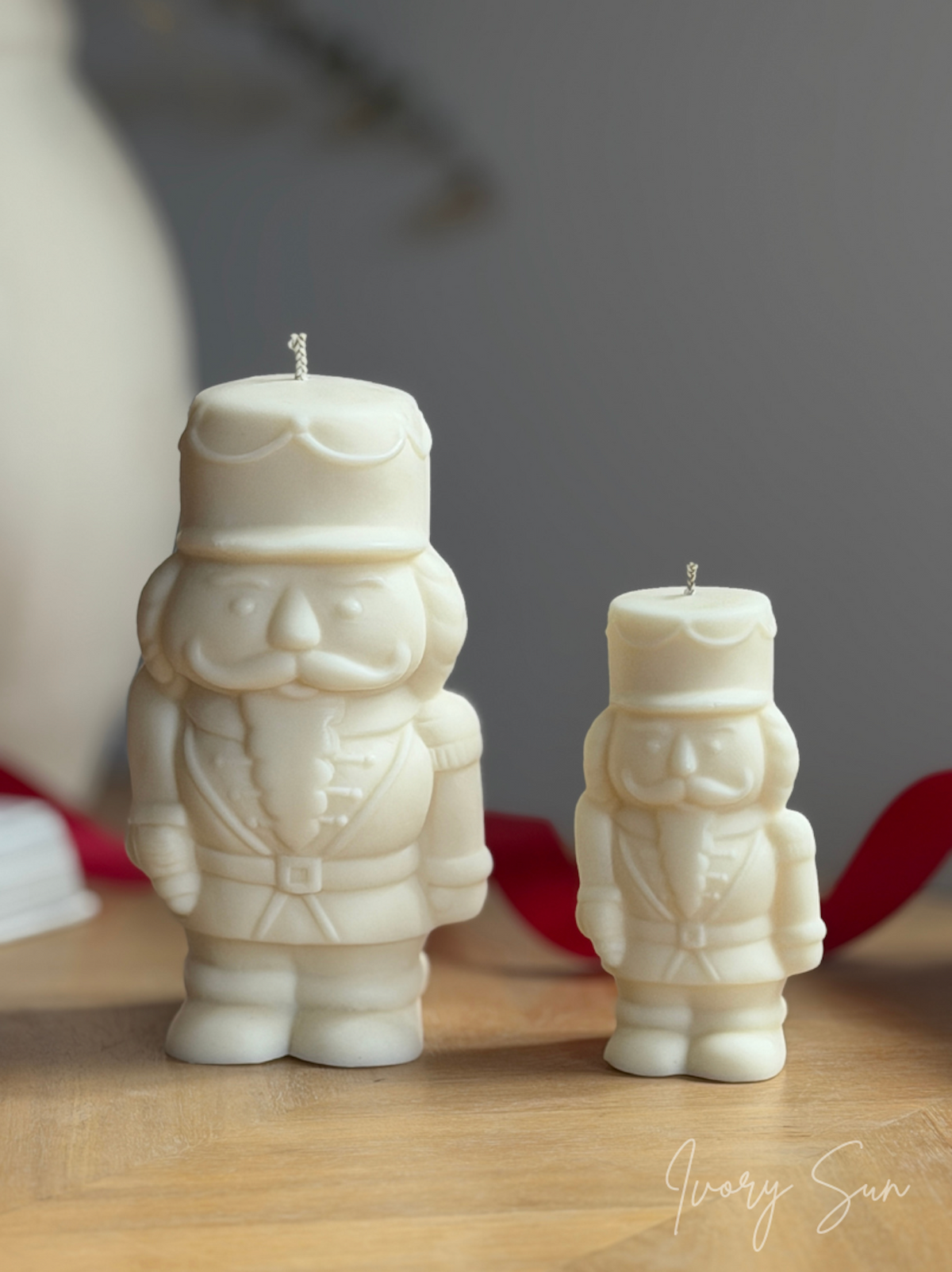 Two off-white Nutcracker Christmas candles, one large and one small, displayed on a light wooden surface with a soft gray background. Handmade Christmas candles by Ivory Sun, beautifully presented as a Christmas gift set. Discover Christmas gift ideas and Christmas Candles in Australia.