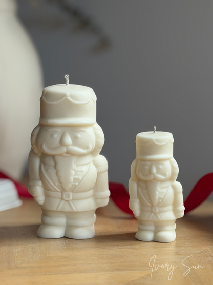 Two off-white Nutcracker Christmas candles, one large and one small, displayed on a light wooden surface with a soft gray background. Handmade Christmas candles by Ivory Sun, beautifully presented as a Christmas gift set. Discover Christmas gift ideas and Christmas Candles in Australia.