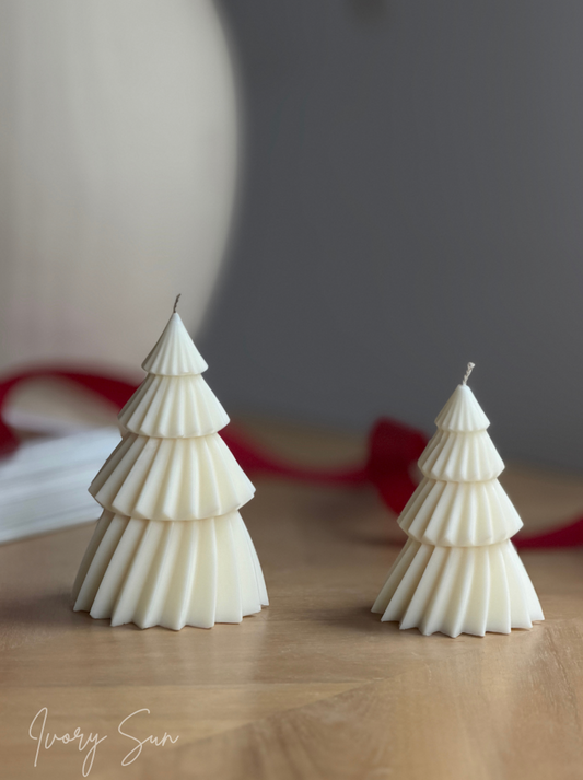 Two white soy Christmas tree shaped candles with pleated detailing, displayed on a light wooden surface with a soft-focus gray background and a red ribbon. Handmade Christmas candles by Ivory Sun, beautifully presented as a Christmas gift set. Discover Christmas gift ideas and Christmas Candles in Australia.