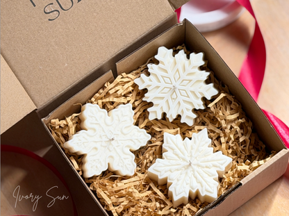 Three white soy snowflake  candles arranged in shredded kraft paper inside an open brown gift box, with a red ribbon visible around the box. Handmade Christmas candles by Ivory Sun, beautifully presented as a Christmas gift set. Discover Christmas gift ideas and Christmas Candles in Australia.